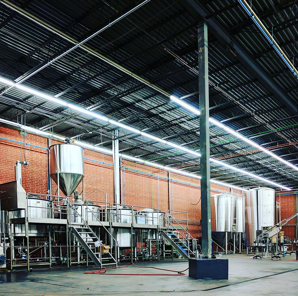 A 30-100 BBL brewhouse set up with all the tanks lined up against a red brick wall.