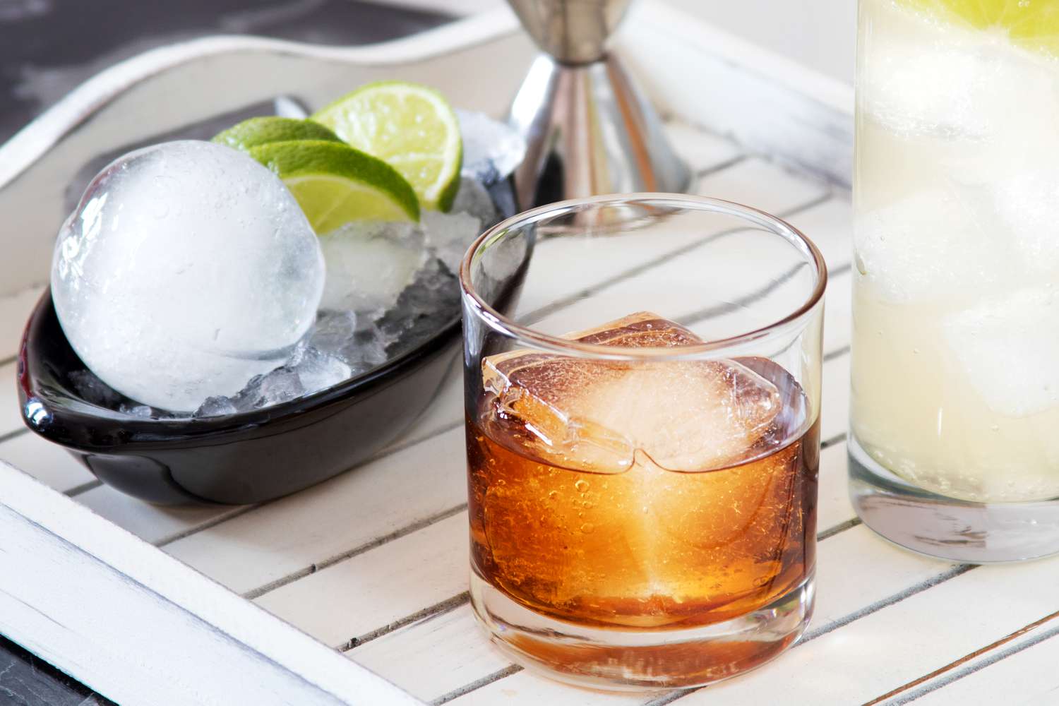 A bowl of ice and cut limes sits beside a glass of whiskey.