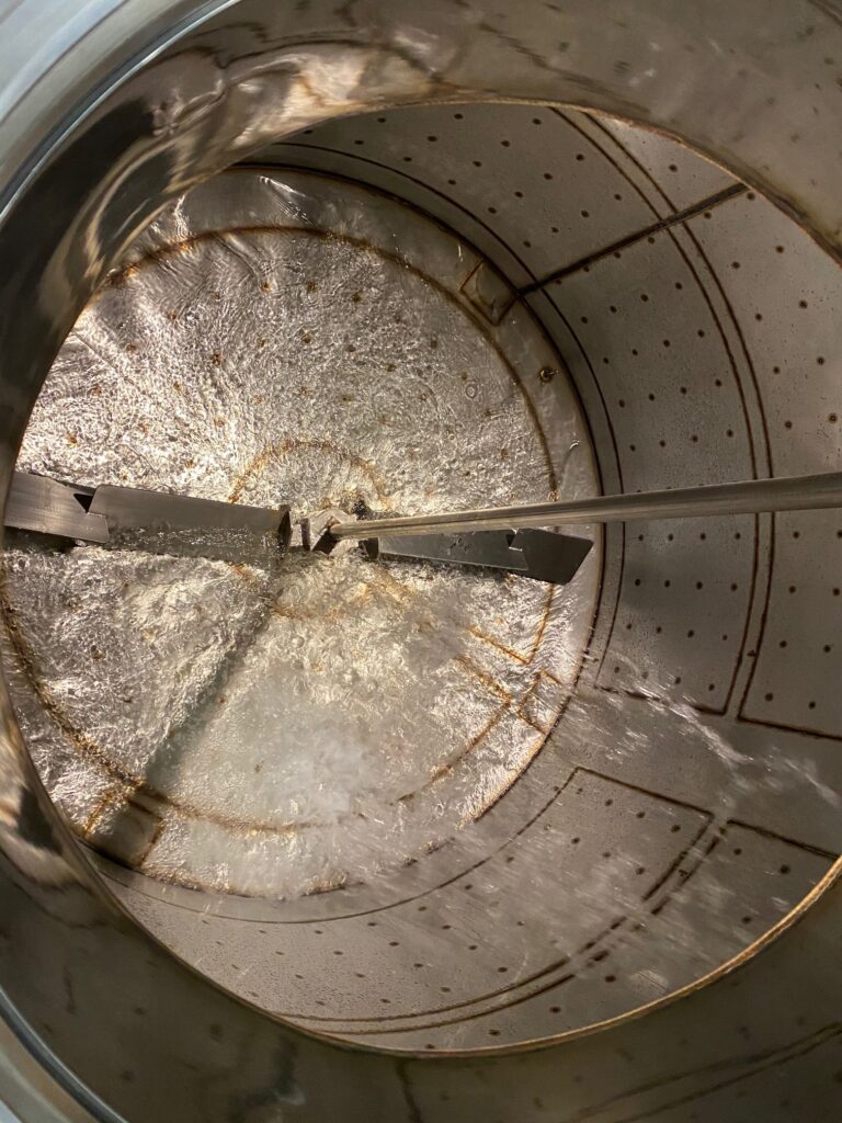 Looking into a tank with a large rake that turns to stir the mash.