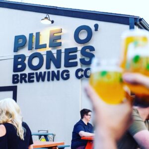 Pile O' Bones brewing Company building with people drinking beer sitting at picnic tables.