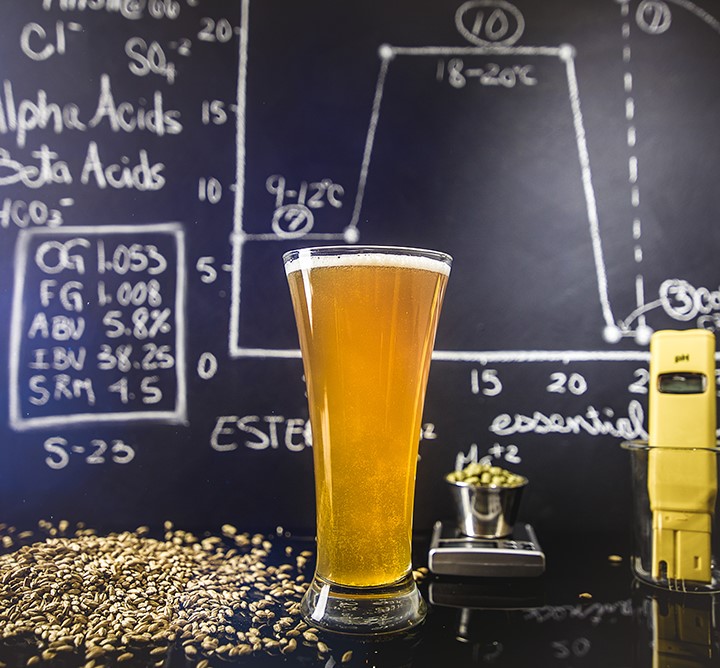 A glass of beer in front of a black chalk board.
